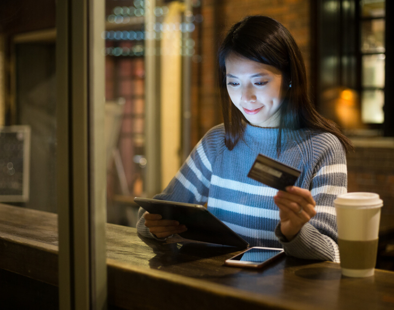 Woman holding her credit card while on her tablet.