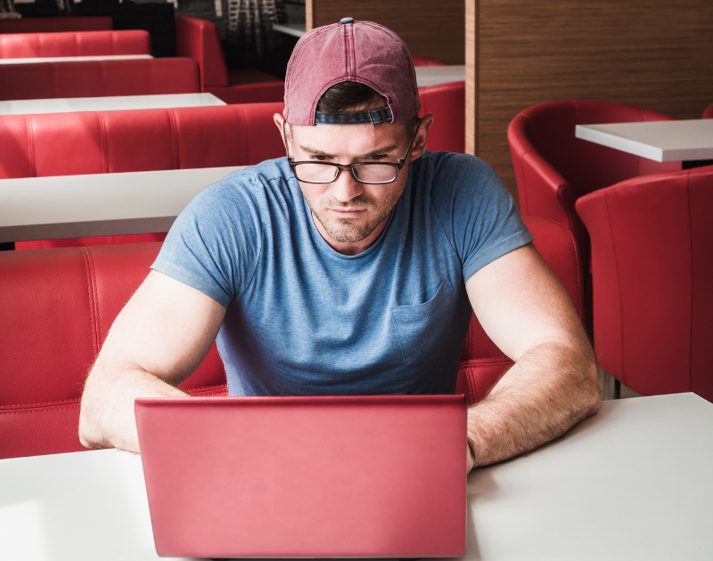 Man in a red booth types on his computer in a concentrated manner. 